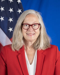 DCM Konick wearing a red jacket standing in front of the U.S. flag